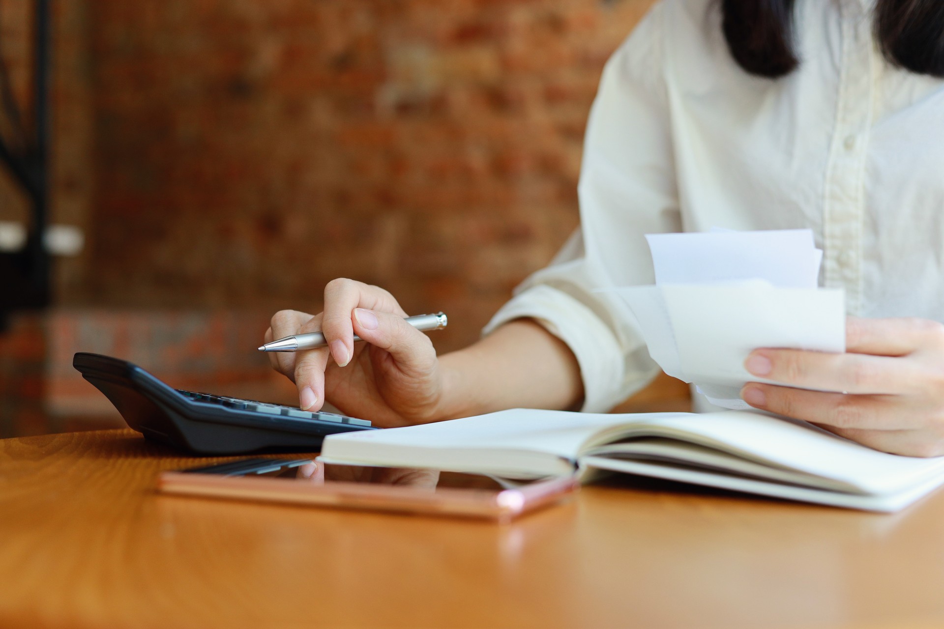 Woman writing a list of debt on notebook calculating her expenses with calculator